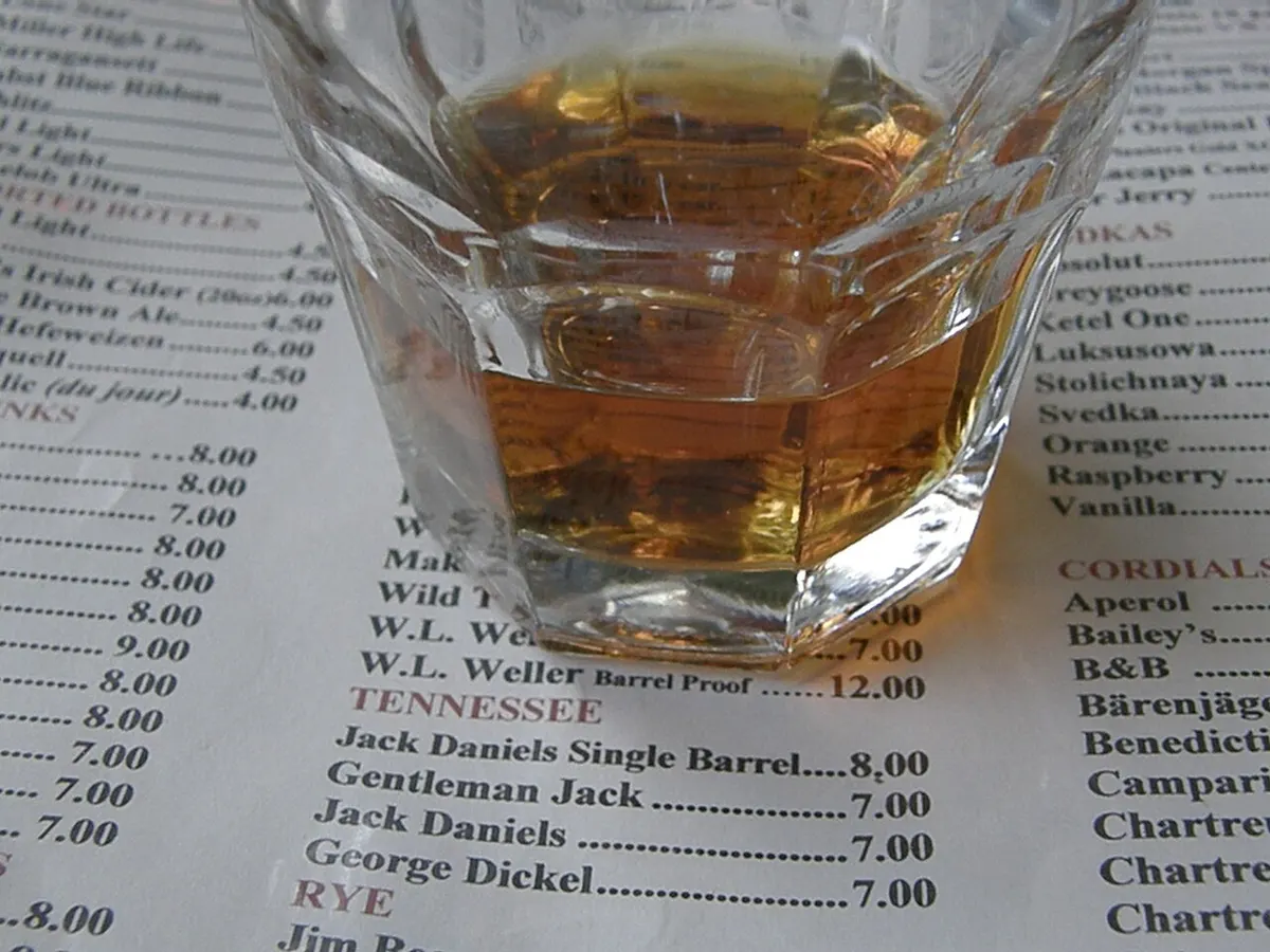 A pour of bourbon whiskey in a tumbler on a wooden bar