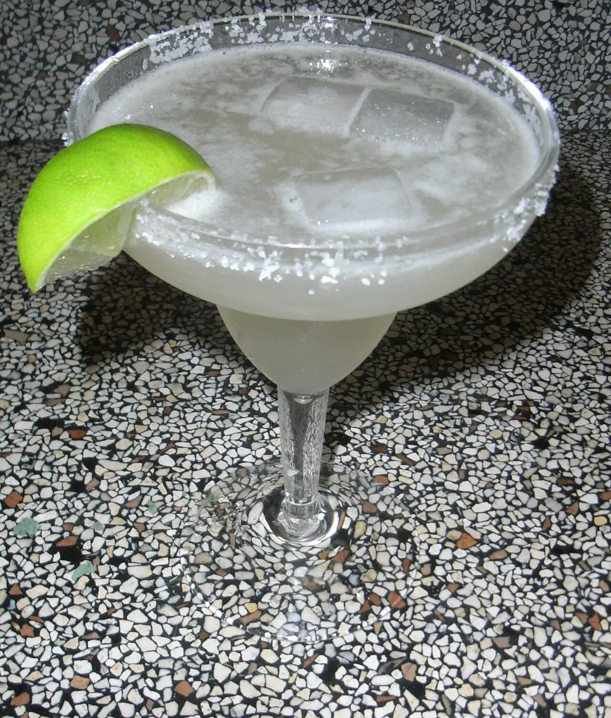 A shaken classic margarita with a salt rim and lime wedge, coarse salt on the glass