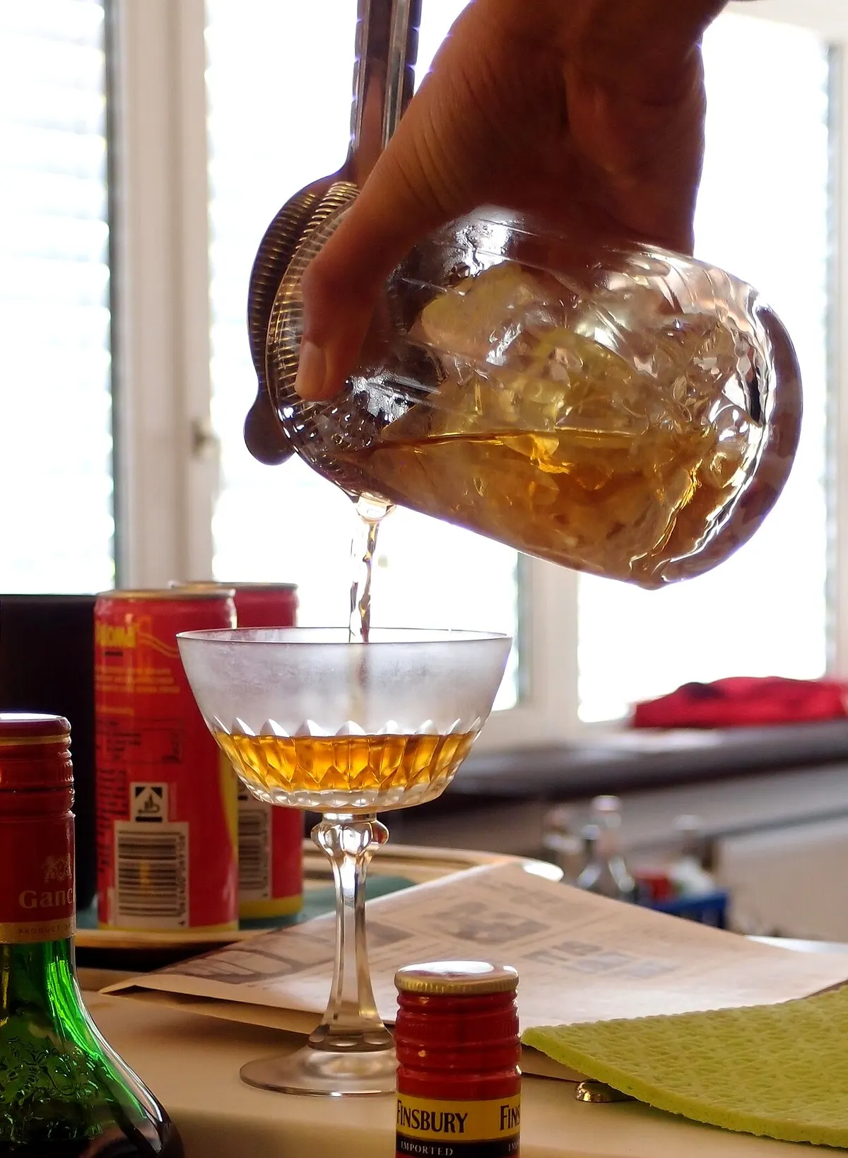 Bartender pouring a stirred cocktail from a mixing glass through a julep strainer