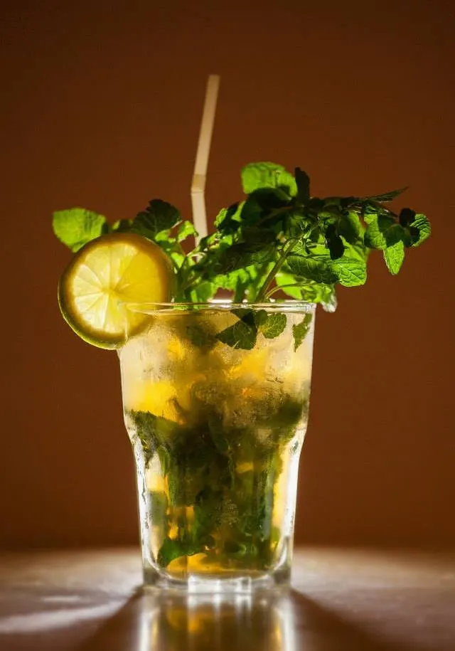 A classic mojito in a highball glass with fresh mint, lime, crushed ice, and a straw