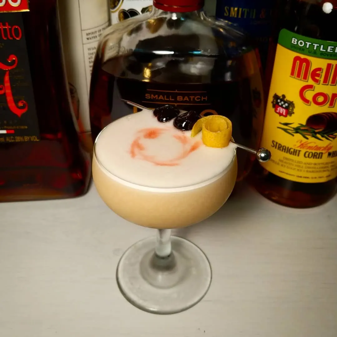 A classic whiskey sour in a coupe glass with an egg white foam cap and a cherry garnish